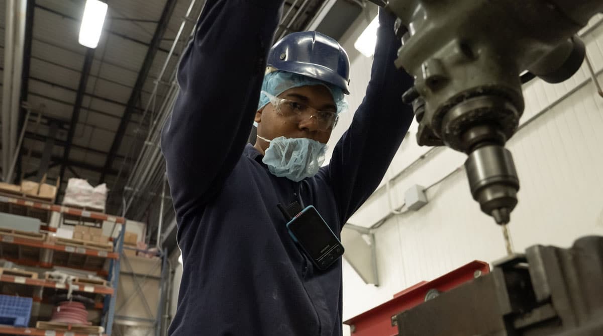 Industrial frontline worker wearing a Walt Smart Radio using an industrial drill.