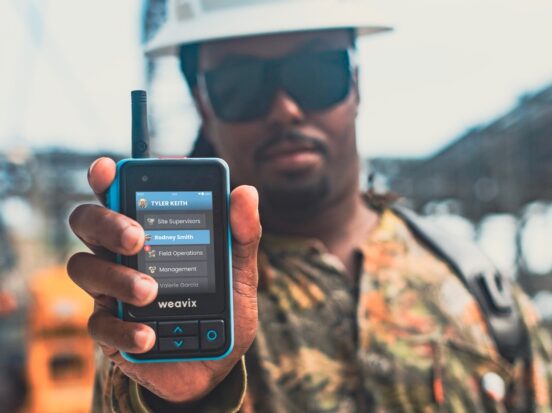 Cover image for a blog on how to build a better frontline employee experience with smart radios. A frontline worker wearing sunglasses and a hard helmet holds up a Walt Smart Radio, with a close-up on all the different channels in their organization.