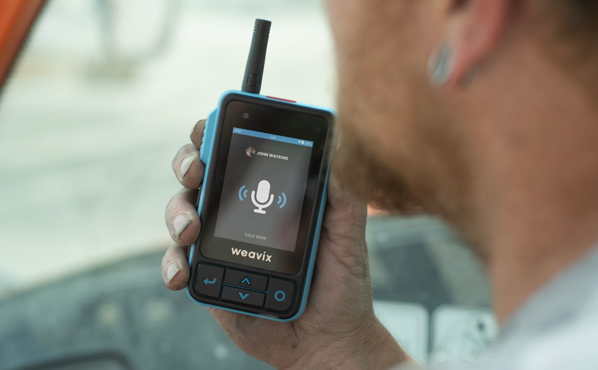 A frontline worker uses the push-to-talk (PTT) capabilities of the Walt Smart Radio to communicate with one of their co-workers. Countless interactions like this one can create a better frontline employee experience on your worksite.